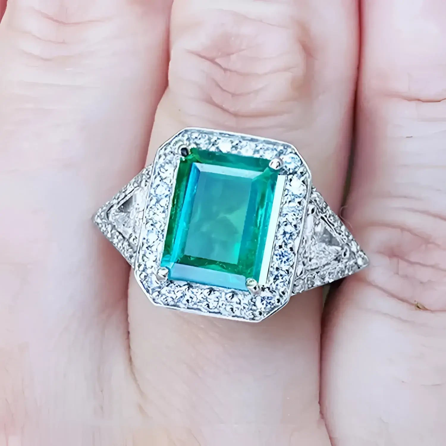 Toma cercana de un anillo con esmeralda cuadrada y diamantes rodeándolo hecho en oro blanco,