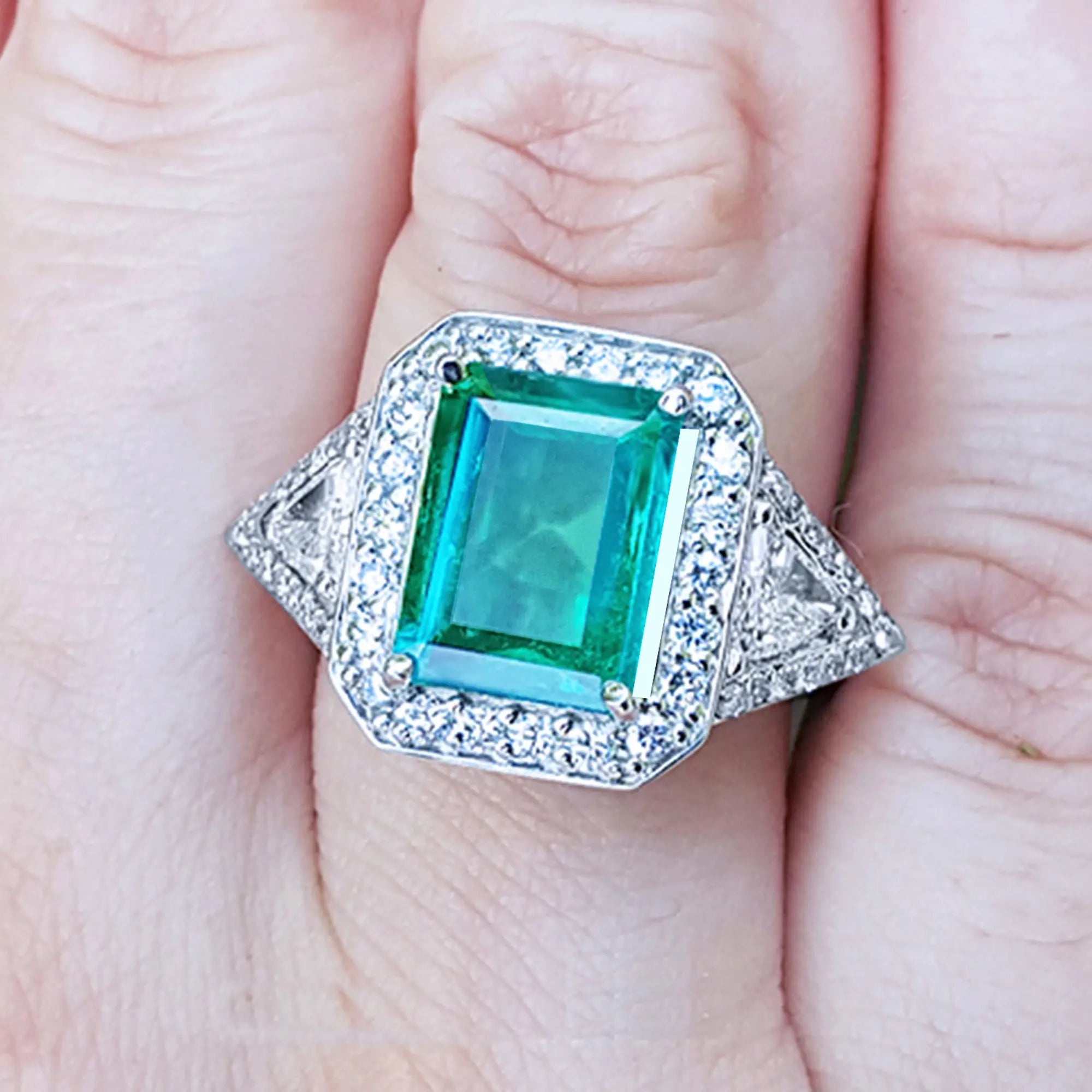 Toma cercana de un anillo con esmeralda cuadrada y diamantes rodeándolo en un dedo.