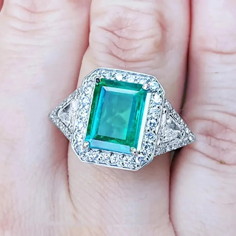 Toma cercana de un anillo con esmeralda cuadrada y diamantes rodeándolo hecho en oro blanco,
