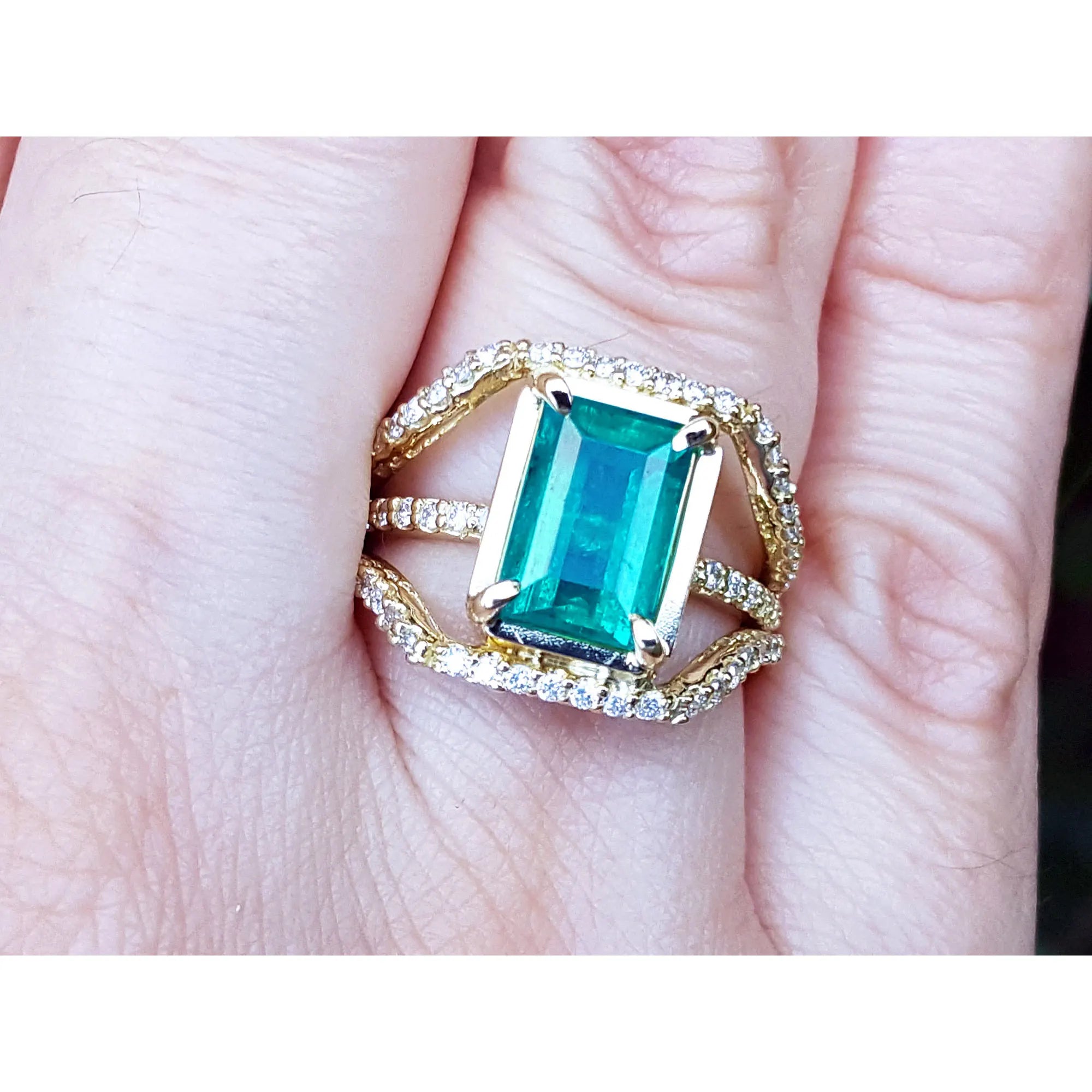 Un deo luciendo un anillo con una esmeralda rectangular sobre tres aros con diamantes.
