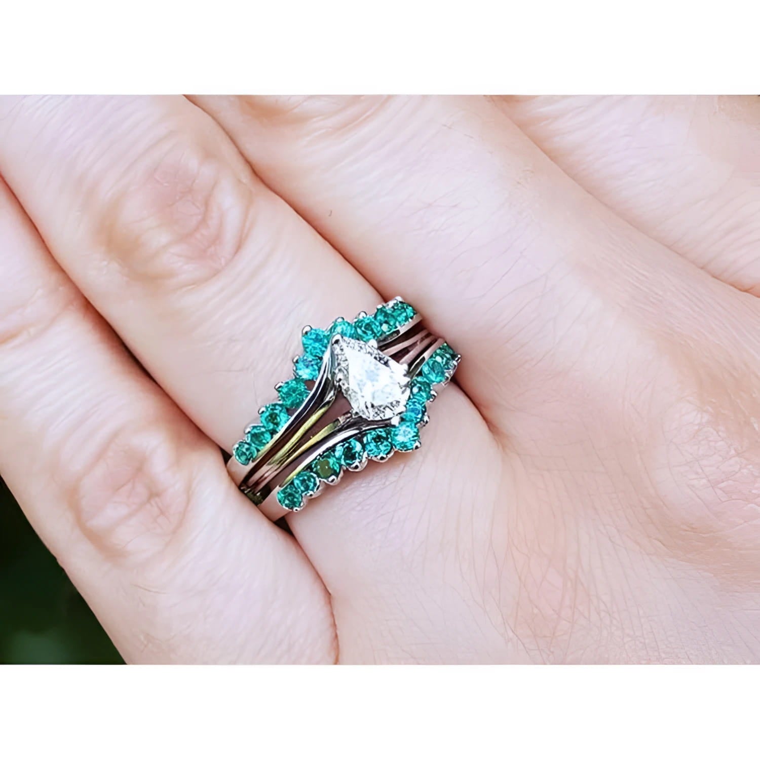 Close-up of a hand wearing an emerald enhancer ring with a central solitaire teardrop diamond ring.