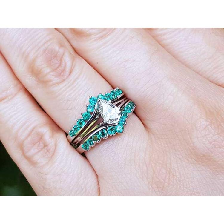 Close-up of a hand wearing an emerald enhancer ring with a central solitaire teardrop diamond ring.