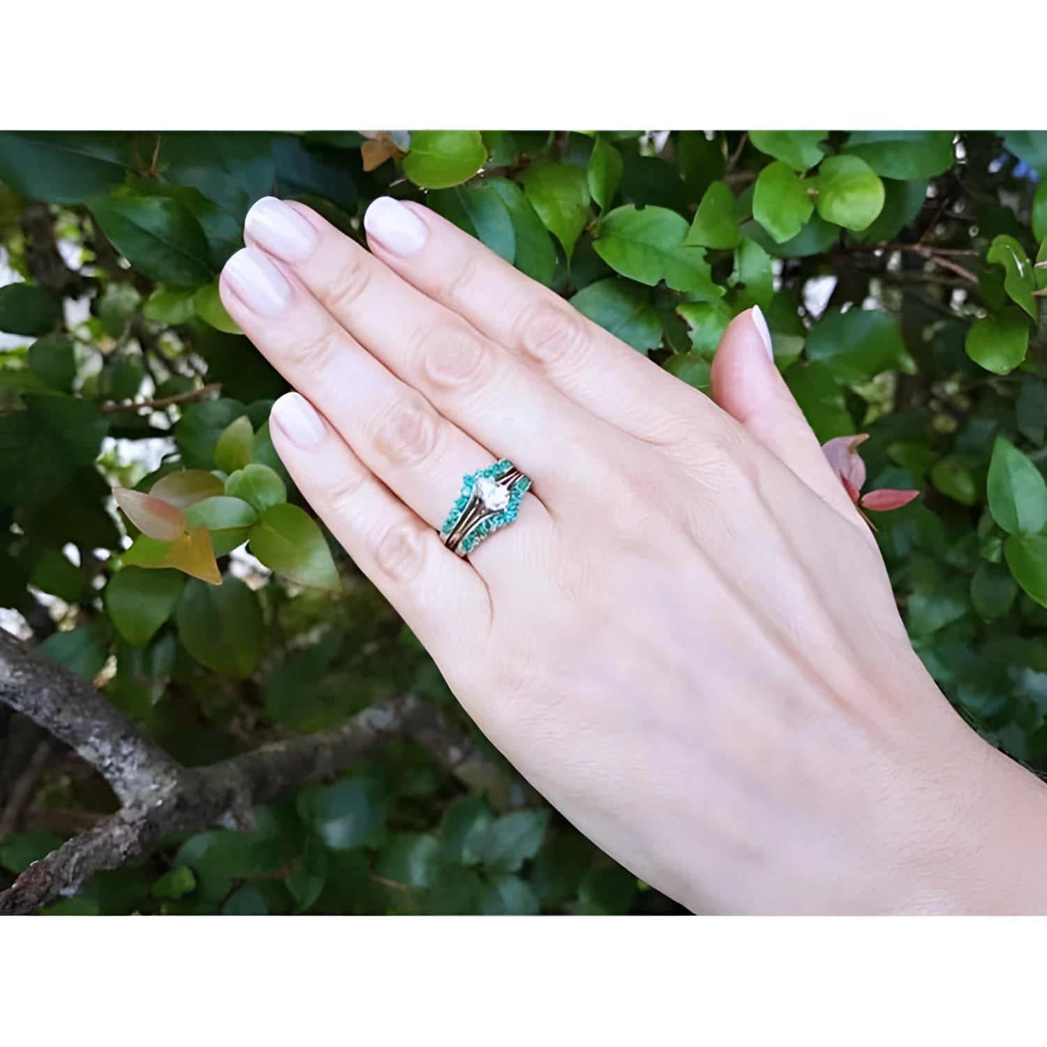 Emerald ring enhancer in 14k white gold with a solitaire ring, worn on a hand against green foliage.
