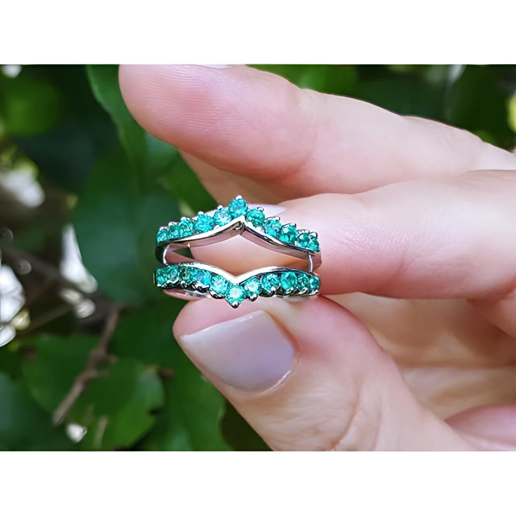 14k white gold ring enhancer with 0.76 ct. round Colombian emeralds, held between fingers.