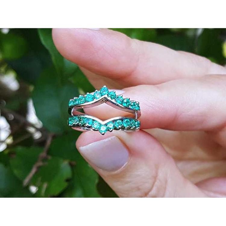 Hand holding a natural emerald enhancer ring with a blurred green leafy background.