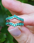 Hand holding a natural emerald enhancer ring with a blurred green leafy background.