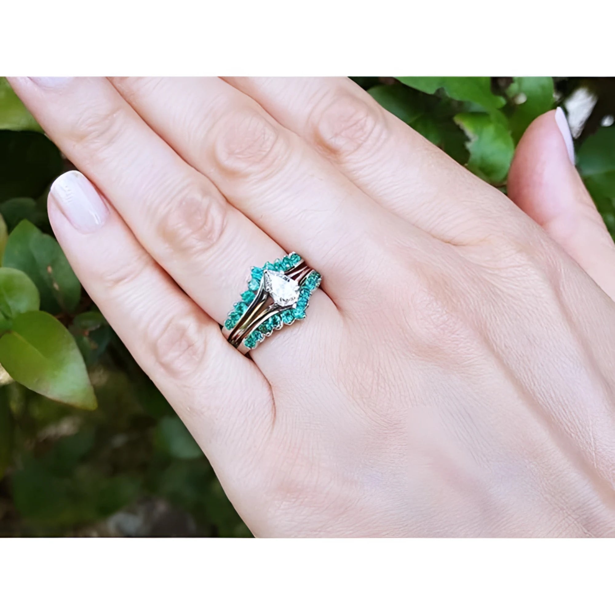 Hand wearing a 14k white gold emerald ring enhancer with 22 round cut Colombian emeralds, surrounding a solitaire ring.