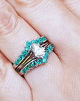Close-up of a hand wearing an emerald enhancer ring with a central solitaire teardrop diamond ring.
