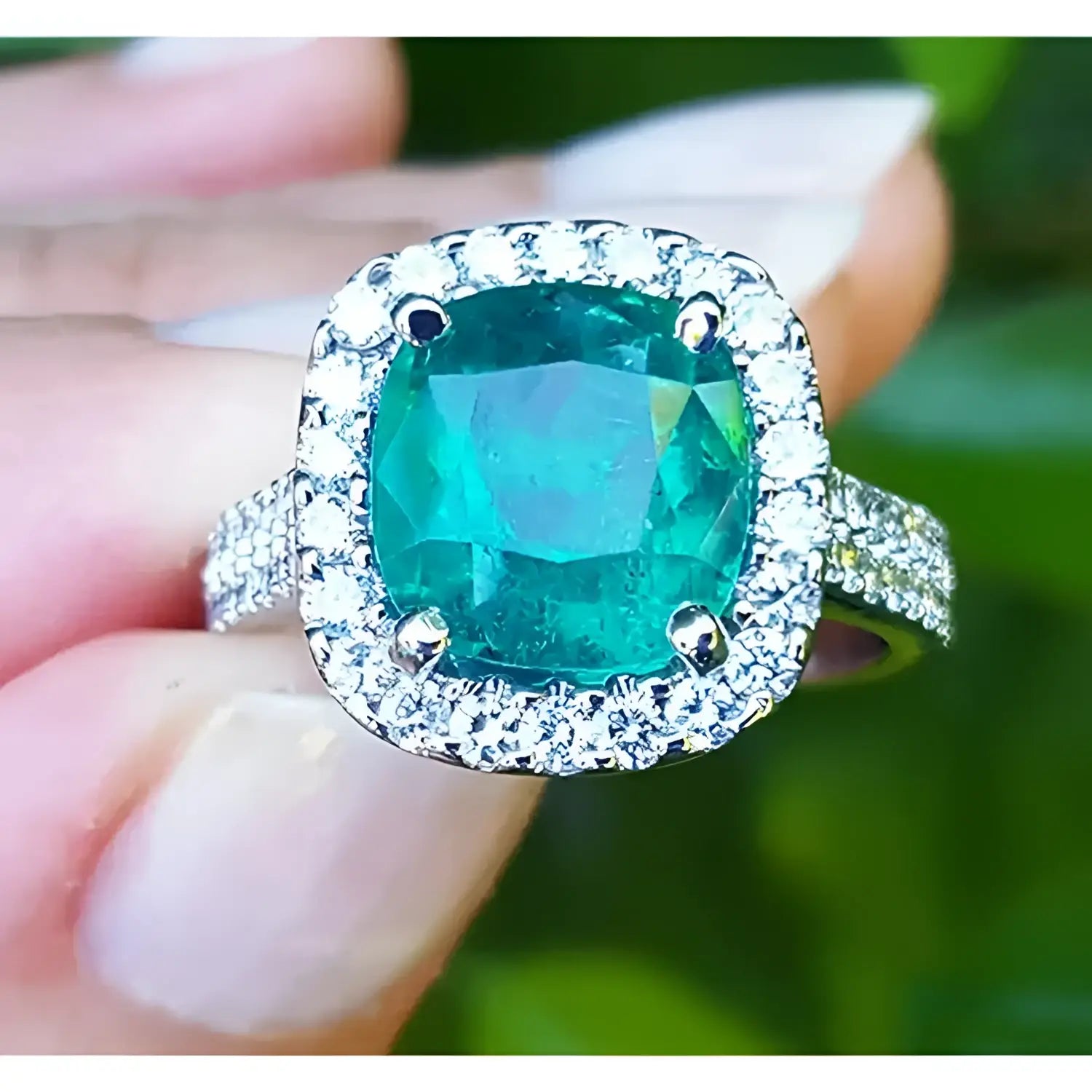 sostenido entre dedos un anillo con esmeralda corte cojín rodeado de diamantes en oro blanco para dama.