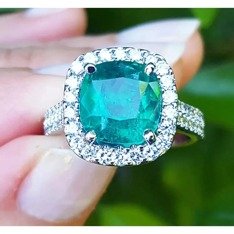 sostenido entre dedos un anillo con esmeralda corte cojín rodeado de diamantes en oro blanco para dama.