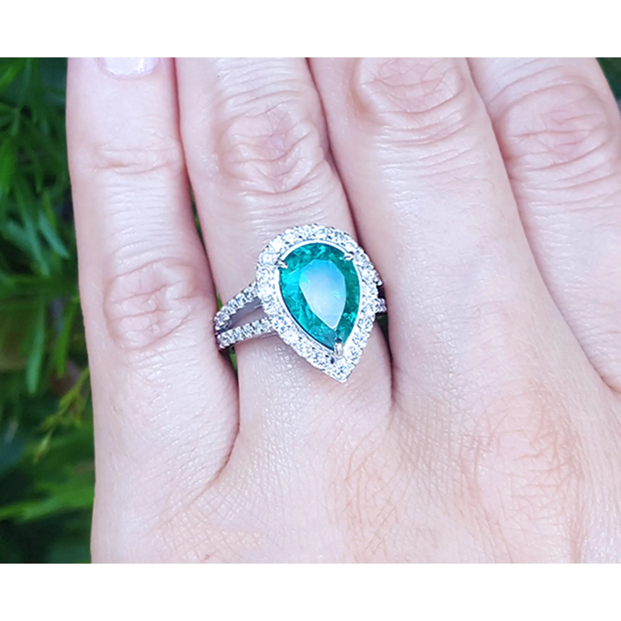 una mano exhibiendo un anillo de oro blanco con una esmeralda corte pera rodeada de diamantes.