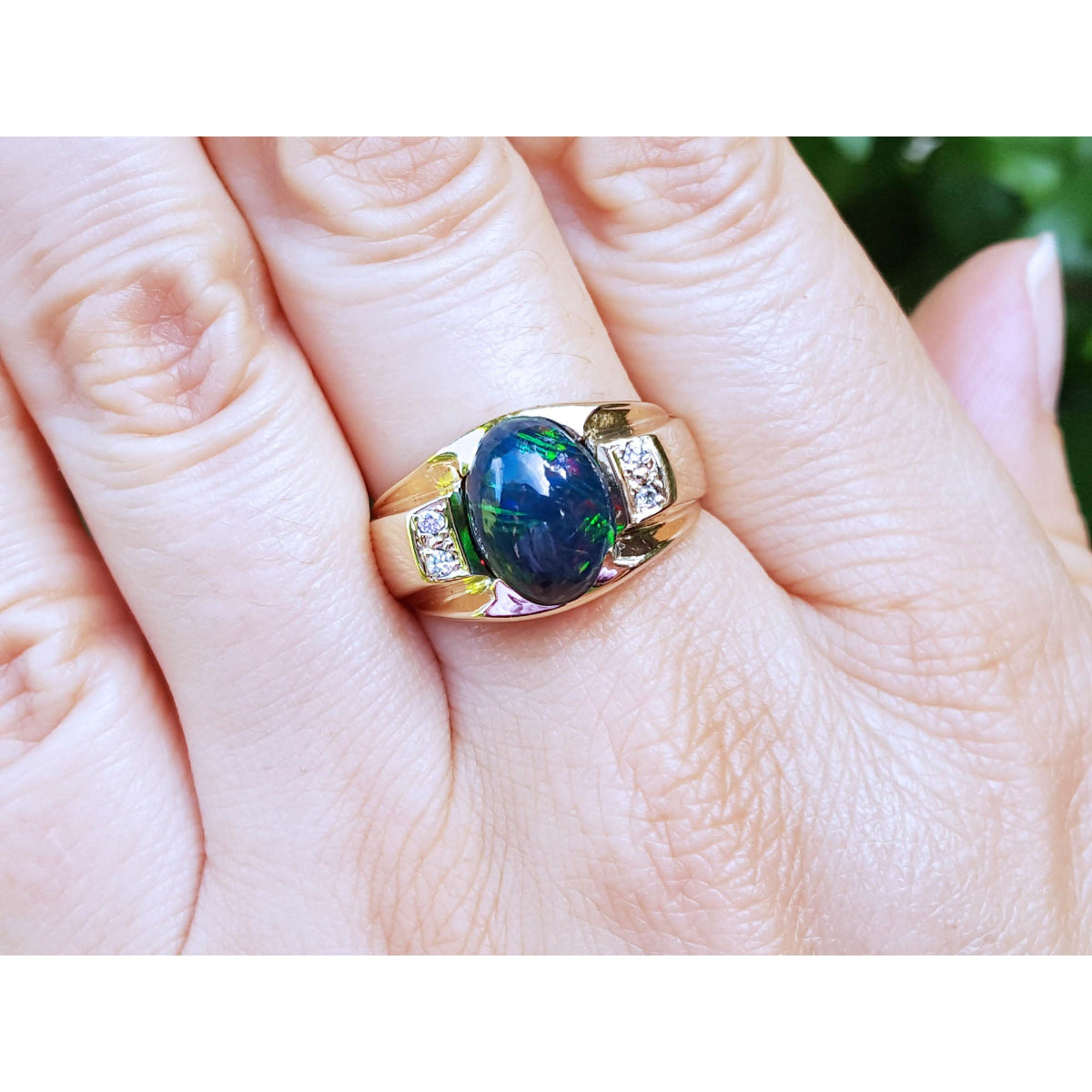 Gold ring with a cabochon black opal on a hand.