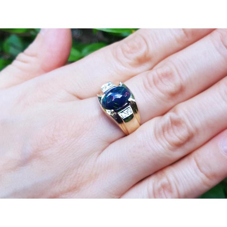 Gold ring with a black opal on a hand against a blurred green background.