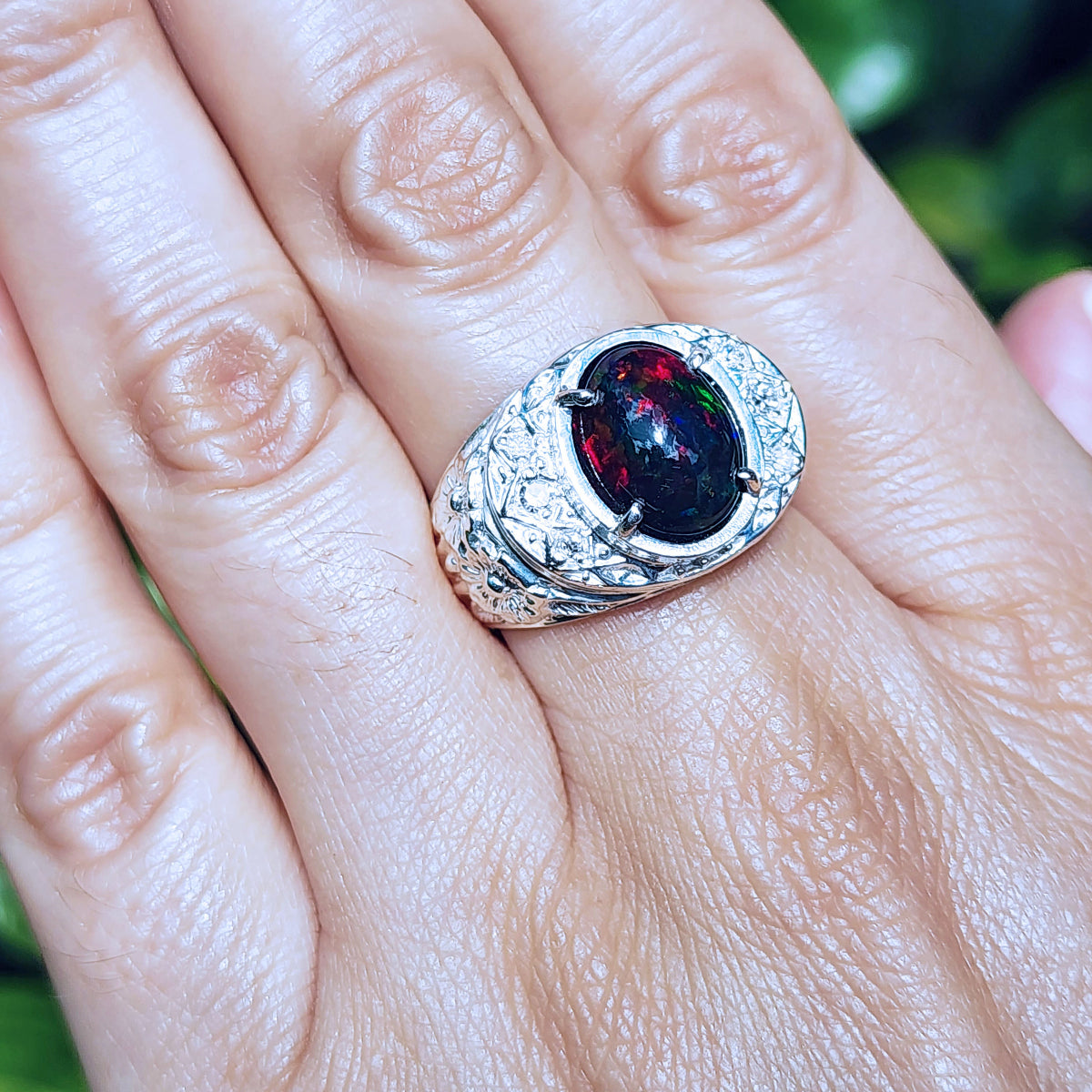 Men's silver ring with a red Welo black opal on a hand against a blurred green background
