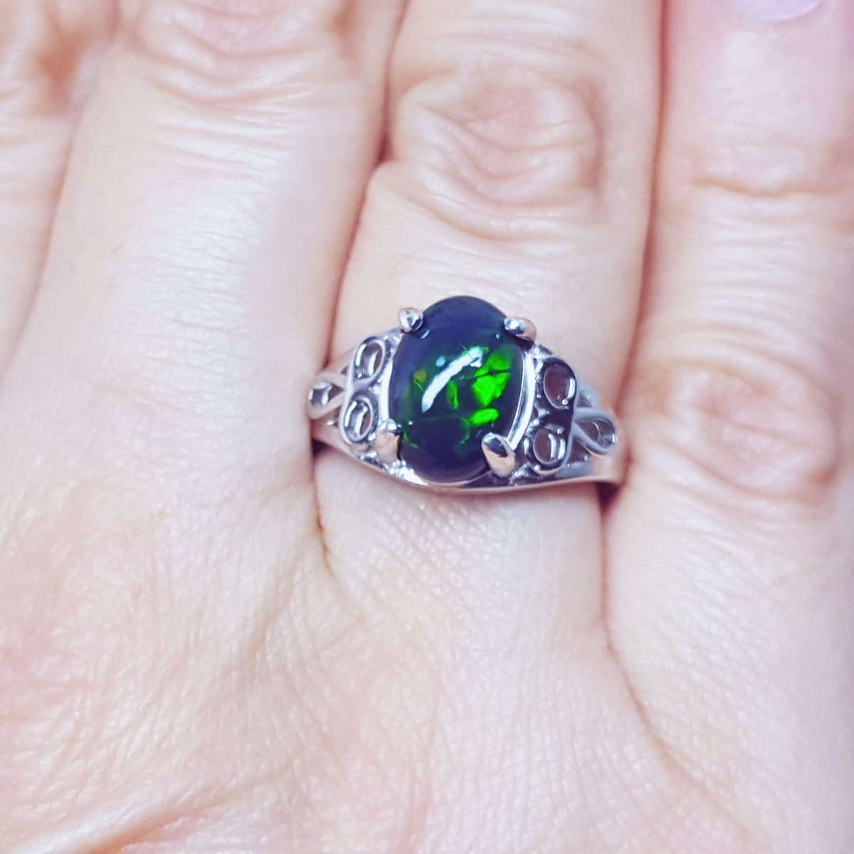 A silver ring with a black opal gemstone on a finger