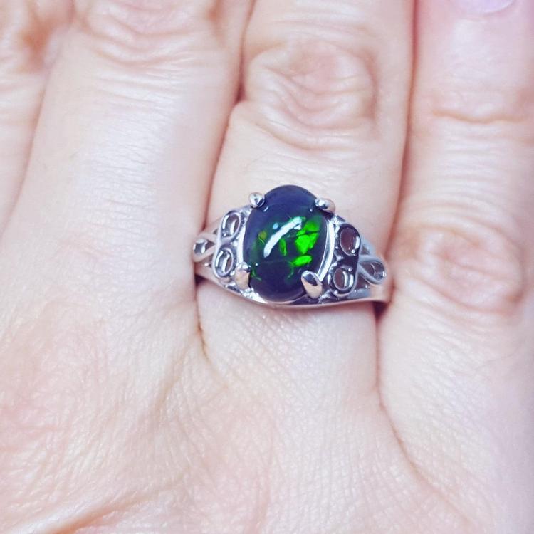 A silver ring with a black opal gemstone on a finger