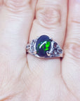 A silver ring with a black opal gemstone on a finger