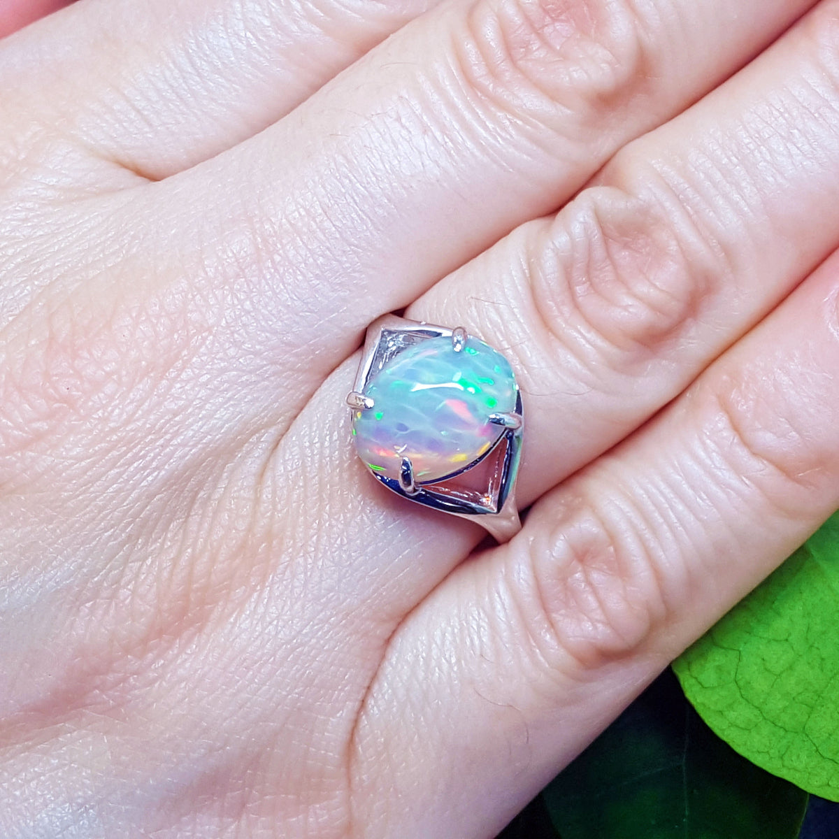 Opal ring on a person&#39;s finger with a green leaf in the background