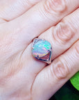 Opal ring on a person's finger with a green leaf in the background
