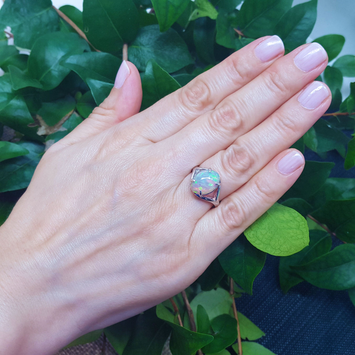 Hand wearing a colorful Ethiopian opal ring with green leaves in the background