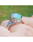 Silver ring with a green opal stone held in a hand against a blurred green background