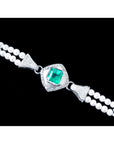 Pearl bracelet with a white gold and diamonds center piece and a square emerald on a black background.