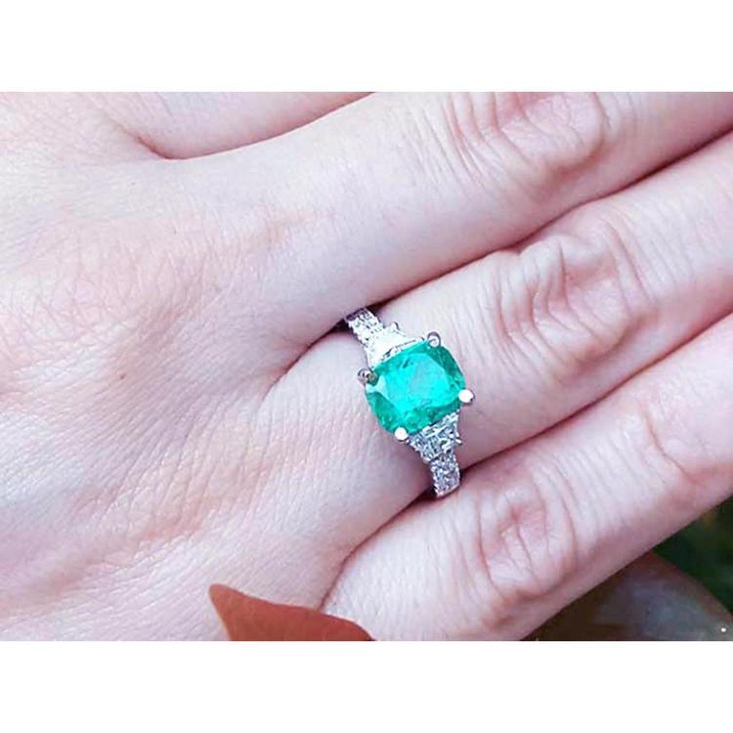 1.90 carat cushion cut emerald ring with trapezoid side diamonds in 18K white gold on a hand.