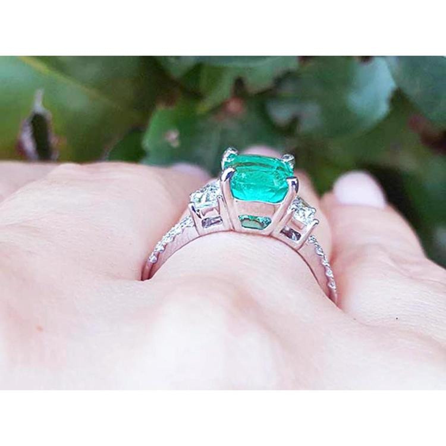 18K white gold ring with a cushion cut emerald and trapezoid side diamonds on a hand.