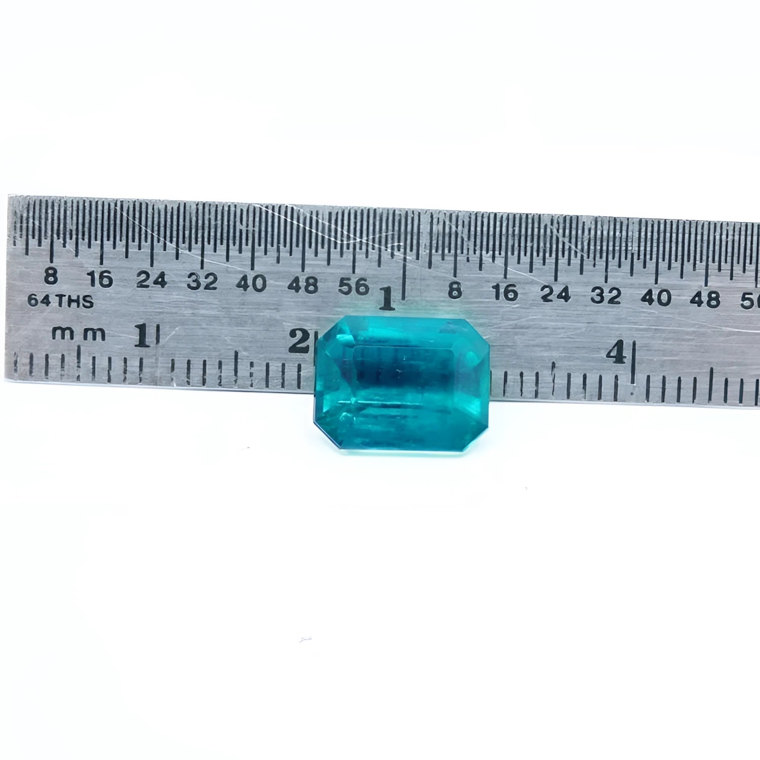 Certified 3.98 ct emerald-cut Muzo emerald with vibrant bluish-green hue, shown next to a ruler for scale.