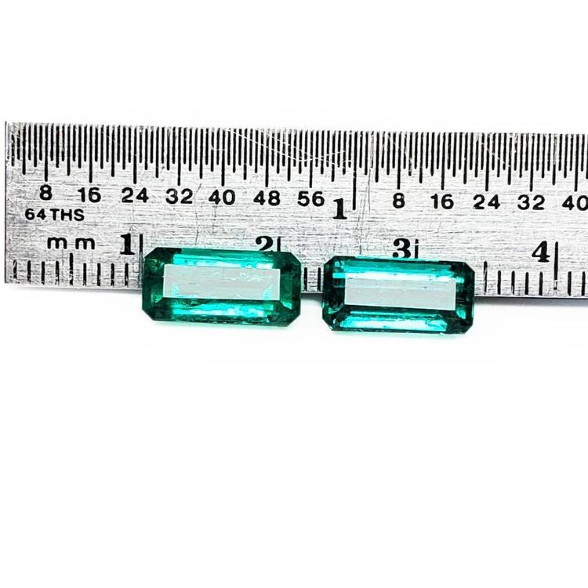 Two emerald-cut, medium deep bluish-green natural emeralds, a matching pair, displayed against a ruler.