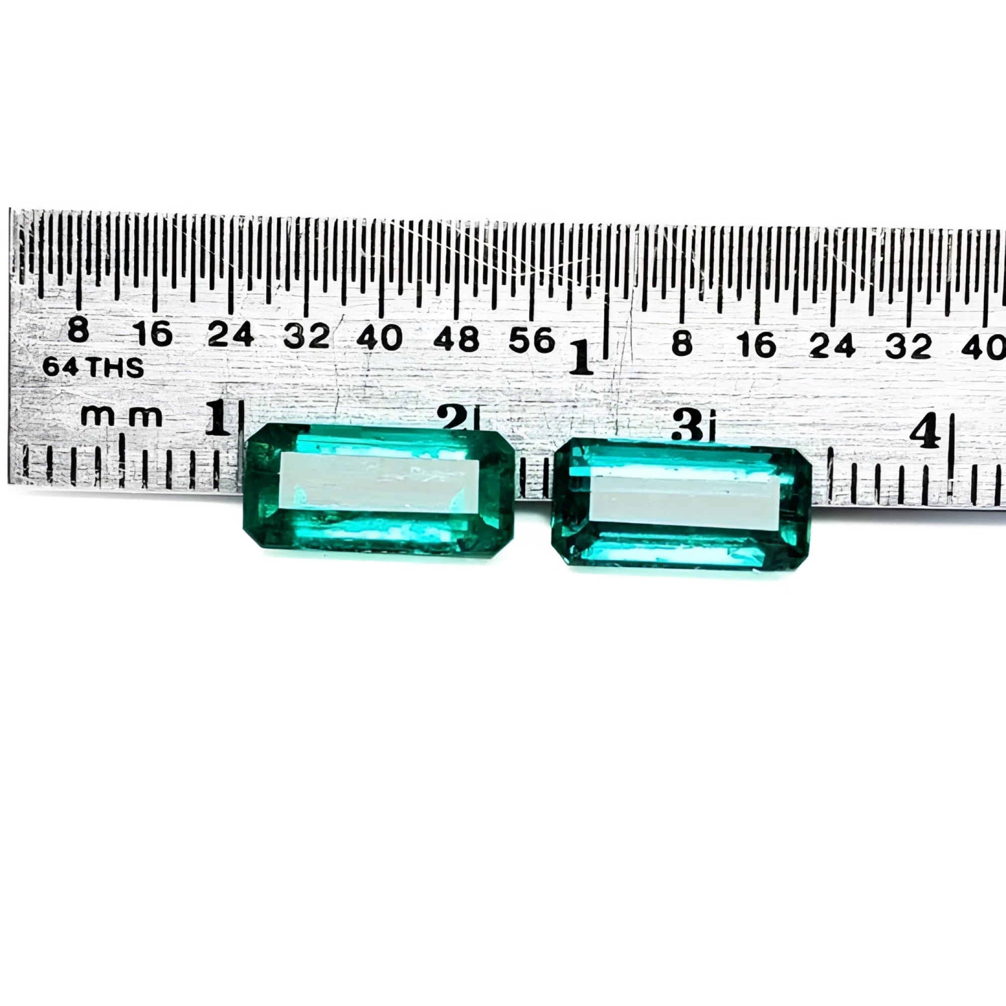 Two emerald-cut, medium deep bluish-green natural emeralds, a matching pair, displayed against a ruler.