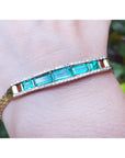 Gold bracelet with five natural emeralds on a wrist against a blurred natural background.