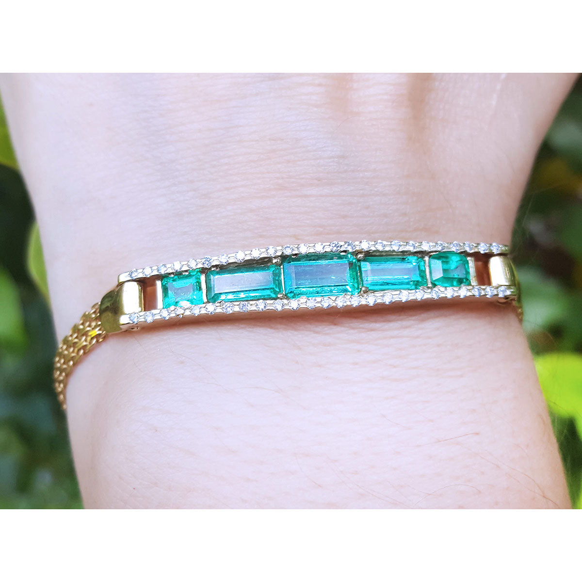 A five stone emerald bracelet natural Colombian emeralds fine quality yellow gold on a wrist against a blurred natural background.