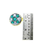 A cufflink with emeralds and diamonds next to a ruler for scale on a white background.