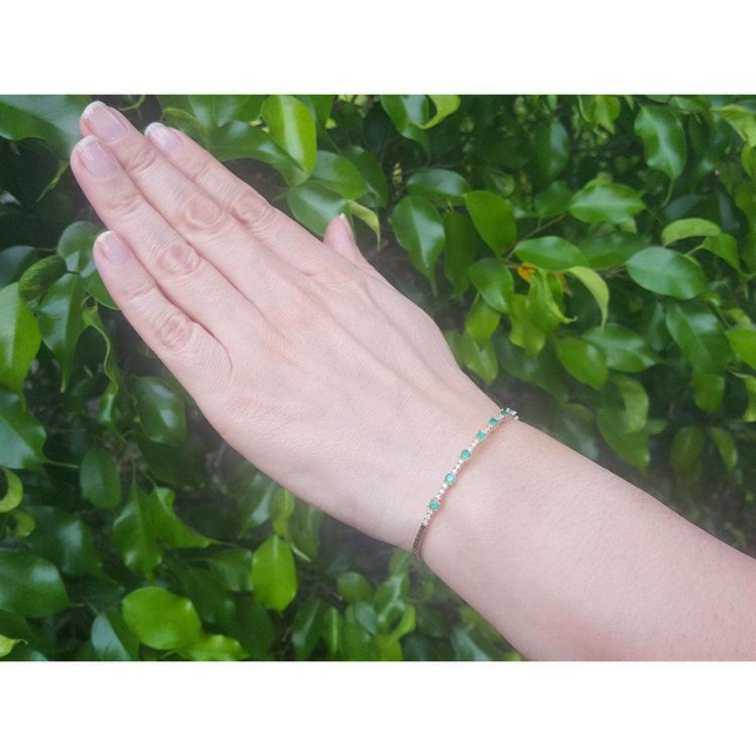 Flexible 14K yellow gold bangle bracelet with genuine emeralds and accent diamonds on a hand.