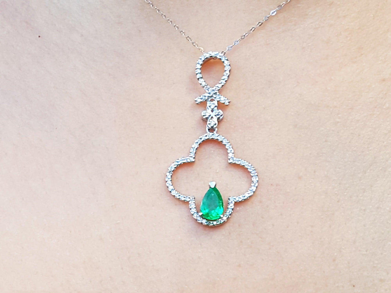 A white gold emerald  pendant with accent diamonds on a beige skin background.