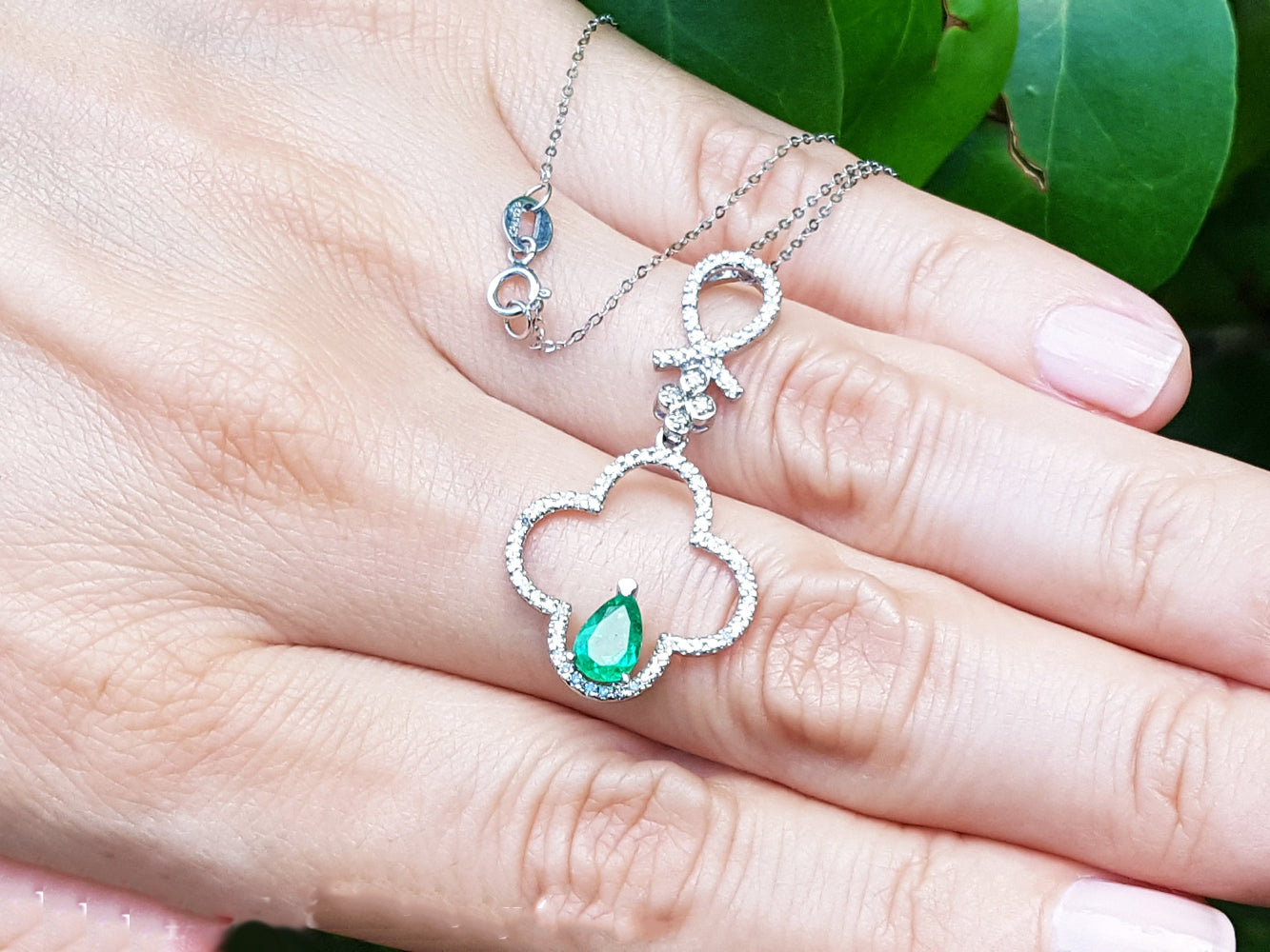A four-leafe pendant with an emerald gemstone on a hand, brand &#39;Emeralds &amp; Jewelry Corp.&#39; visible