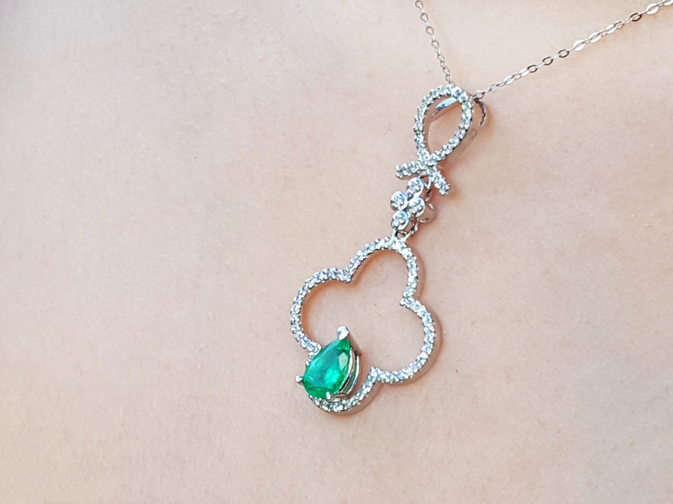 A white gold necklace with a four-leafe pendant and emerald gemstone on a beige background.