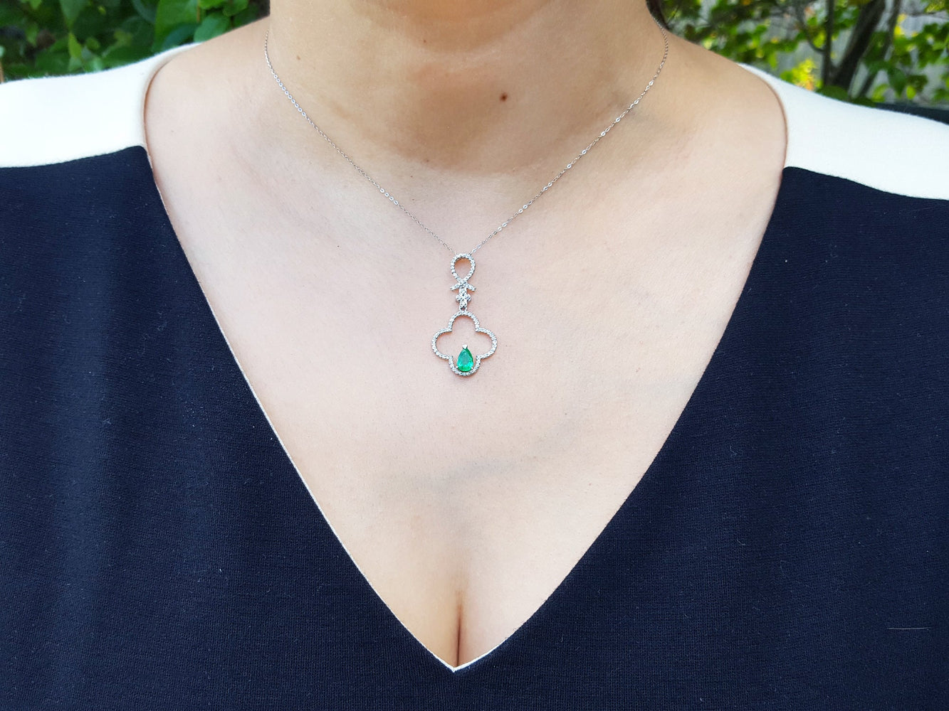 Necklace with a emerald pendant worn by a woman against a blurred natural background.