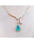 Frontal close view of a necklace with a teardrop-shaped emerald gemstone pendant on a lady's collar