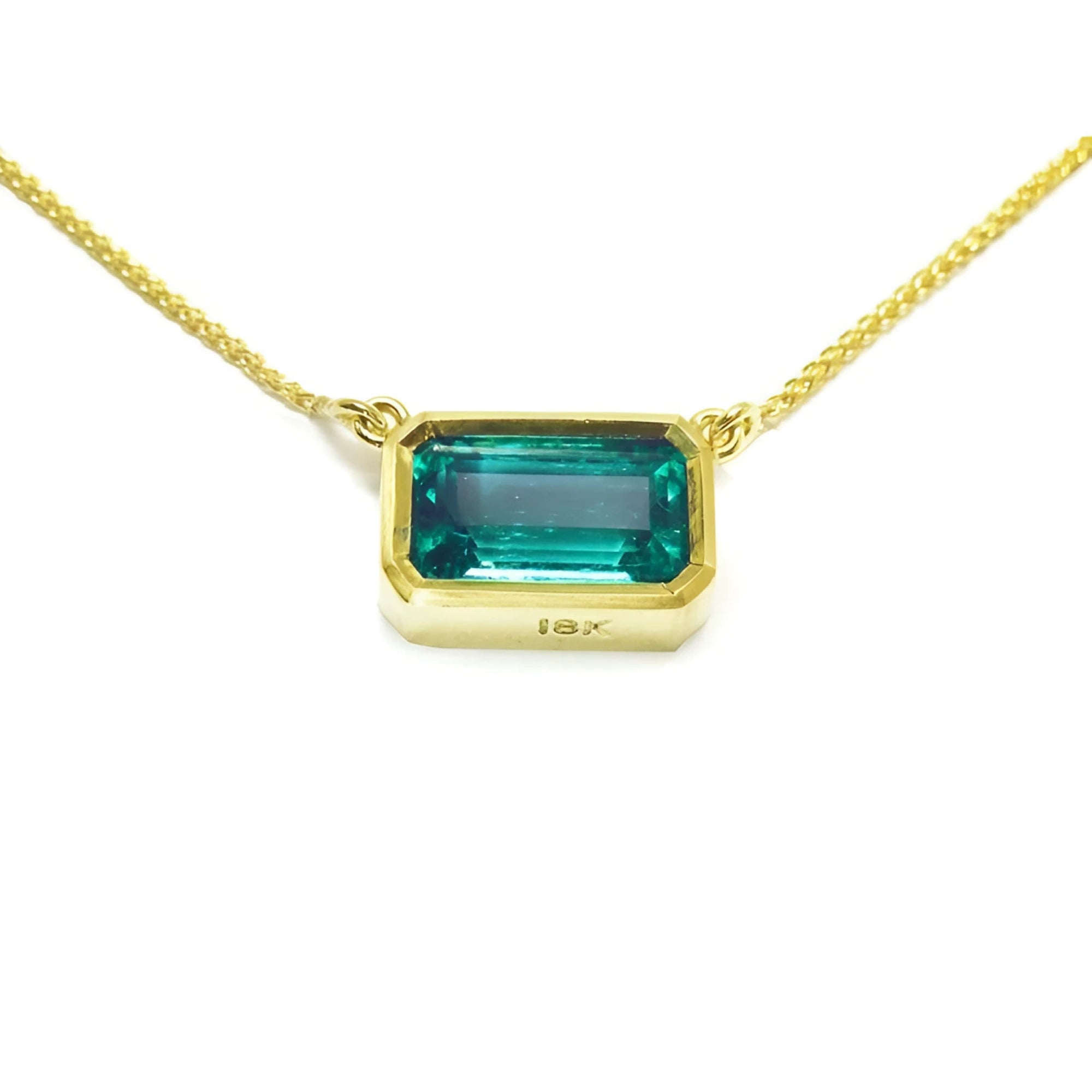East-west rectangular emerald solitaire necklace in 18K yellow gold with a vibrant bluish-green stone.