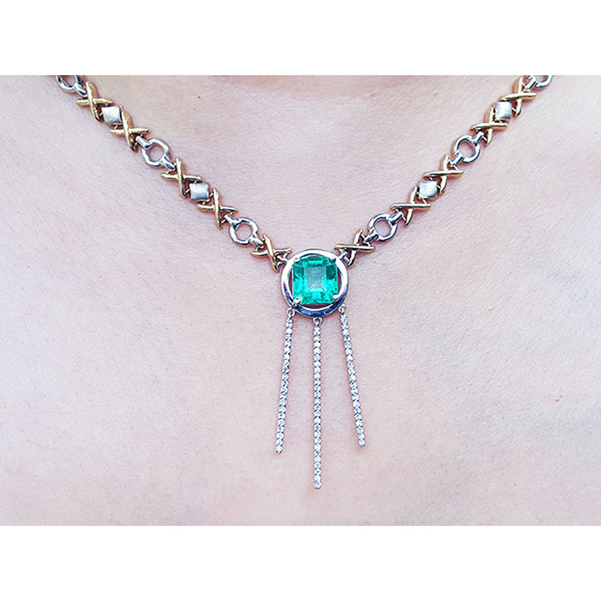 close frontal view of a kisses and hugs necklace with a natural emerald gemstone on a white background