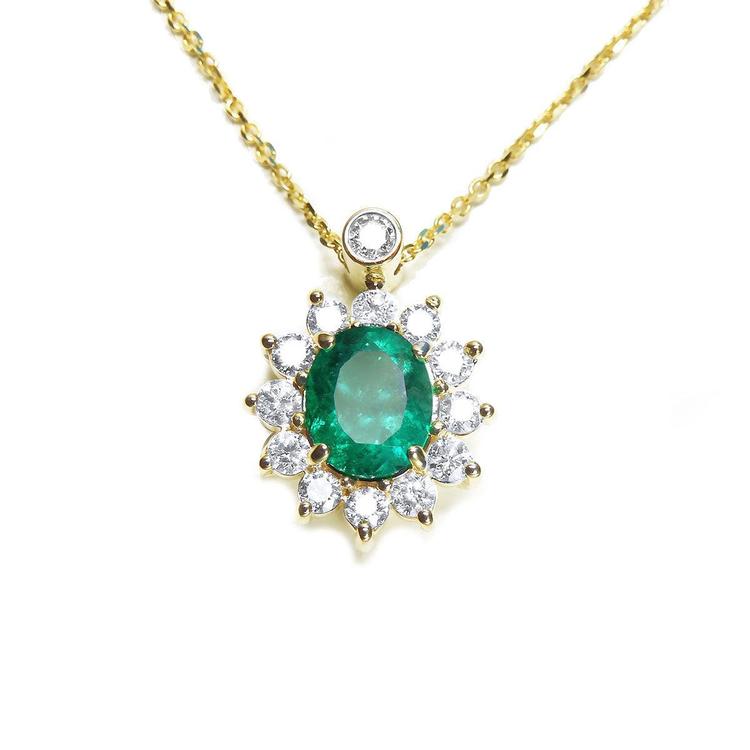 Front view of a gold necklace with an oval emerald in a halo diamond pendant on a white background