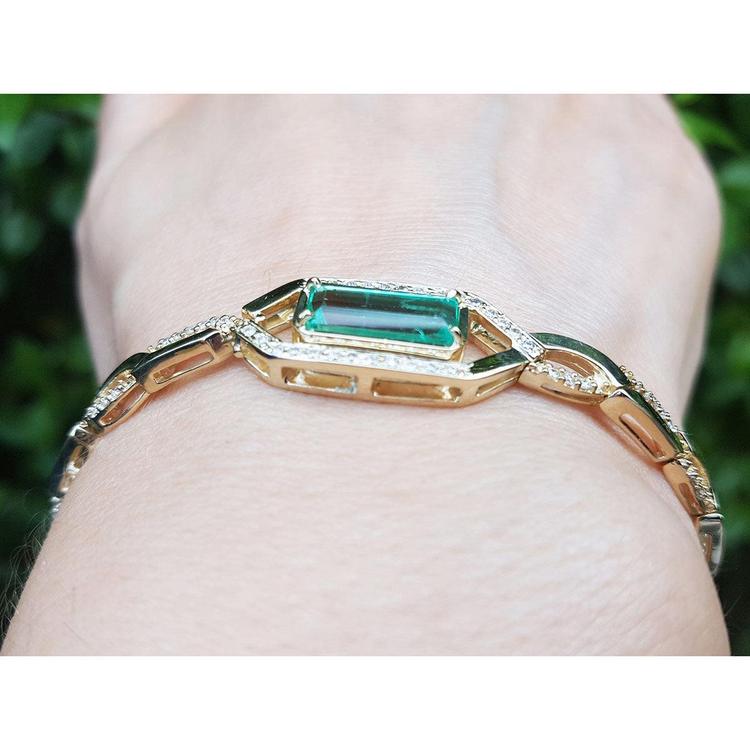 Gold bracelet with a real colombian emerald on a person's wrist against a blurred green background