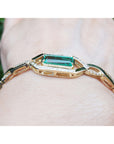 Gold bracelet with a real colombian emerald on a person's wrist against a blurred green background