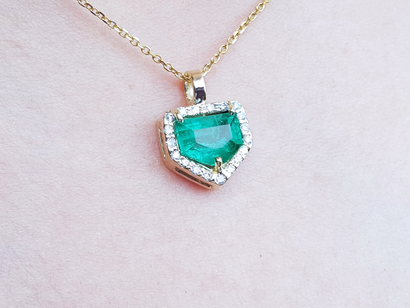 Gold necklace with a heart-shaped emerald pendant on a light pink background