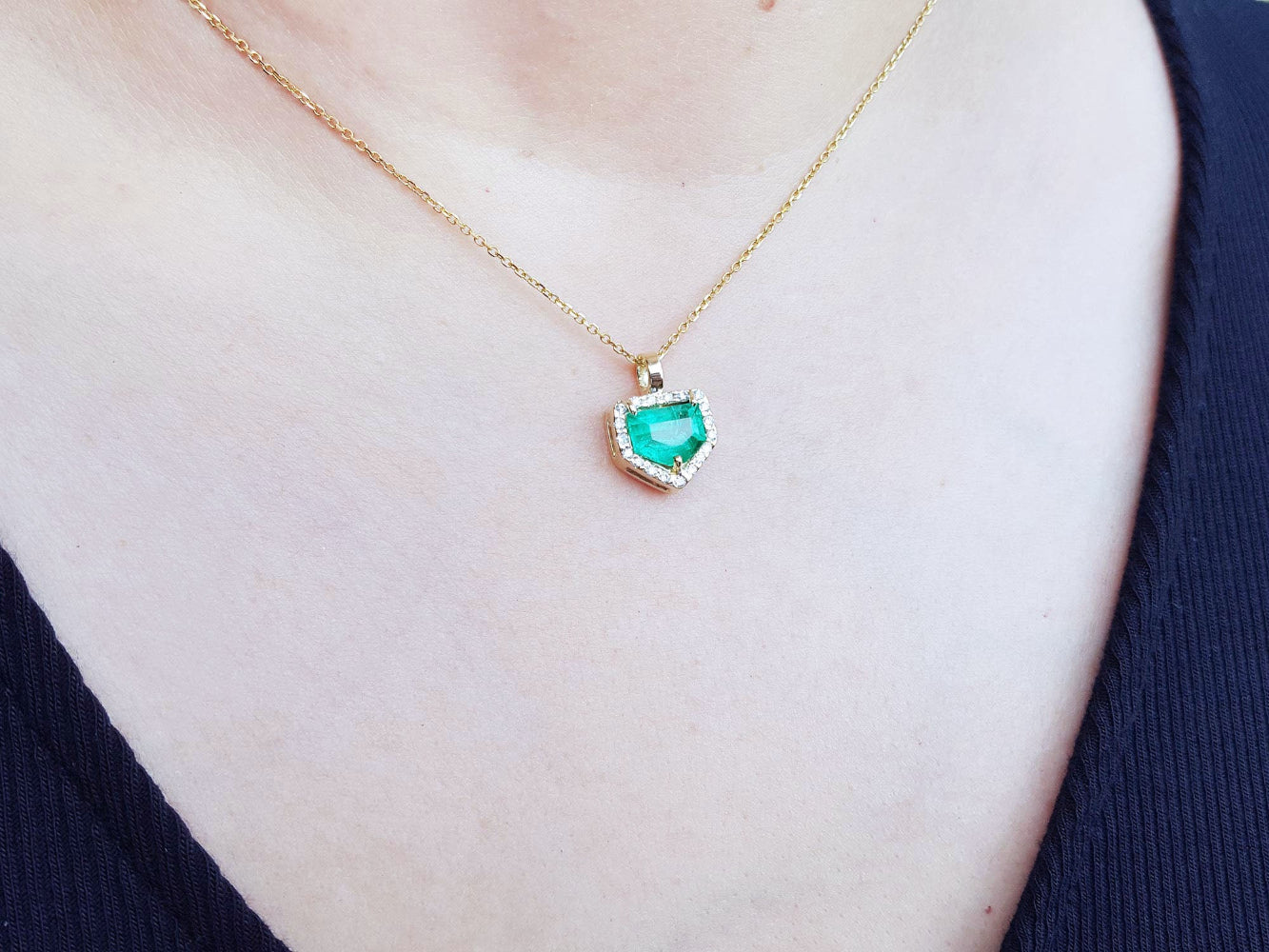 Necklace with a heart-shaped natural emerald pendant on a person wearing a dark blue top.