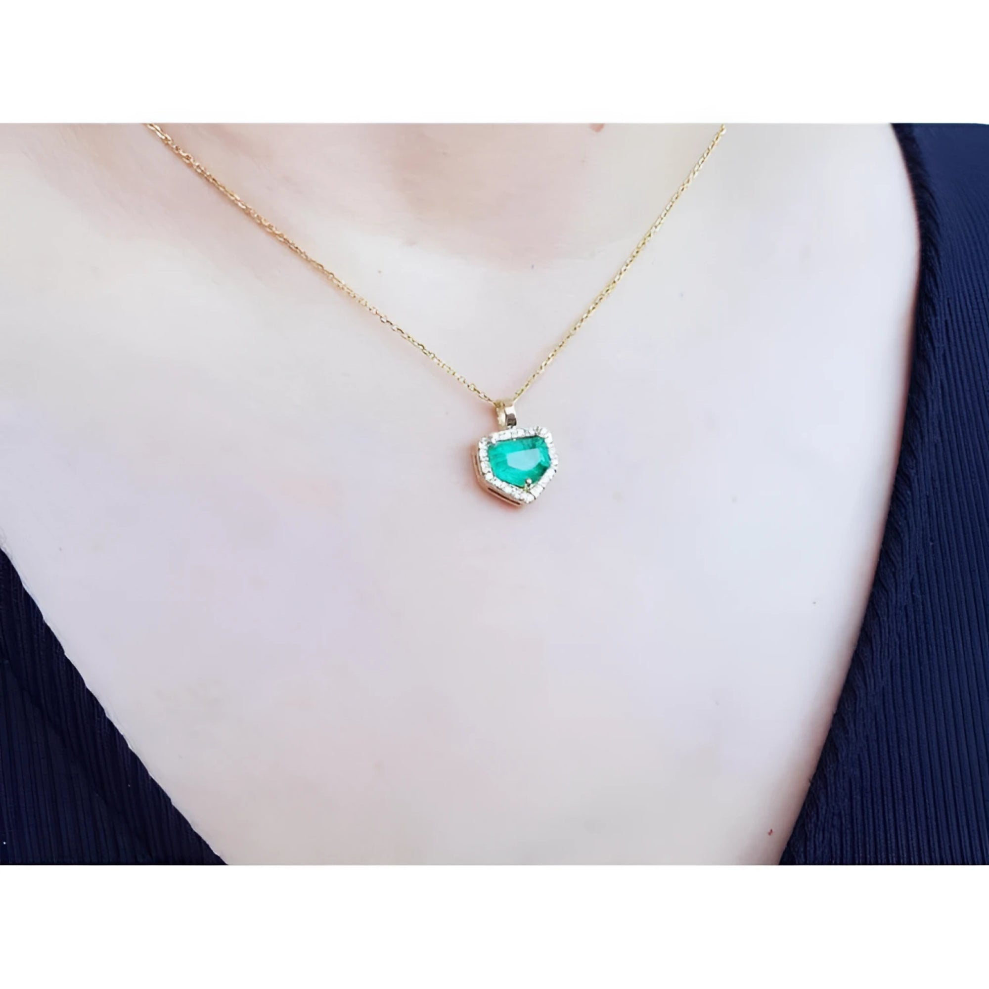 Colombian emerald pendant with diamond halo on a thin 14K gold chain, worn on a person.