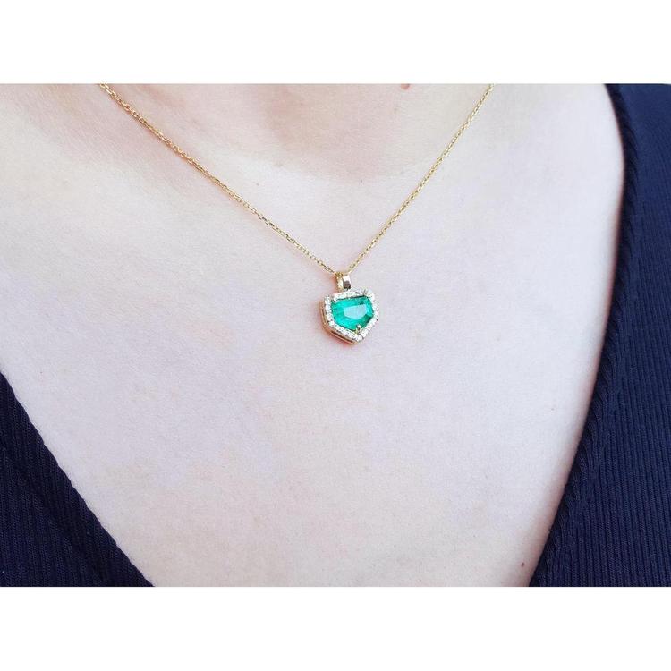 Colombian emerald pendant with diamond halo on a thin 14K gold chain, worn on a person.