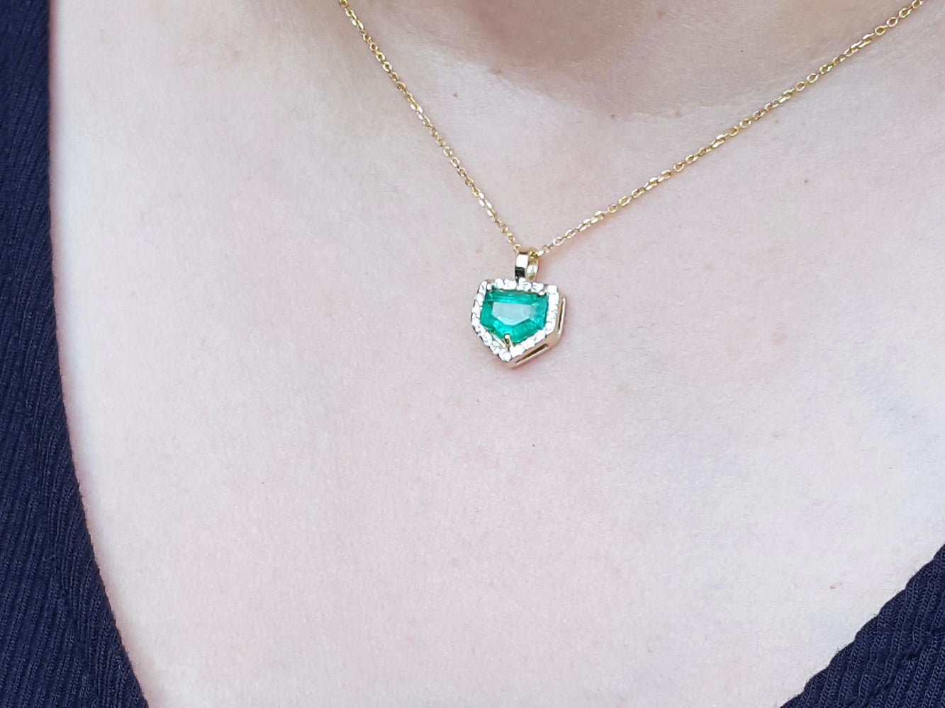 Gold necklace with a heart-shaped emerald pendant on a blurred background.